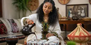 A woman performing an Ethiopian coffee ceremony, pouring coffee from a jebena into cups in a traditional setting.